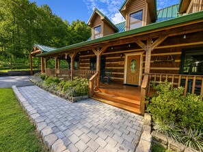 A wooden cabin with a porch, a covered outdoor seating area, and a stone pathway leading to the entrance. - Dogwood Acre 3 Bedroom Cabin by RedAwning (Sevierville)