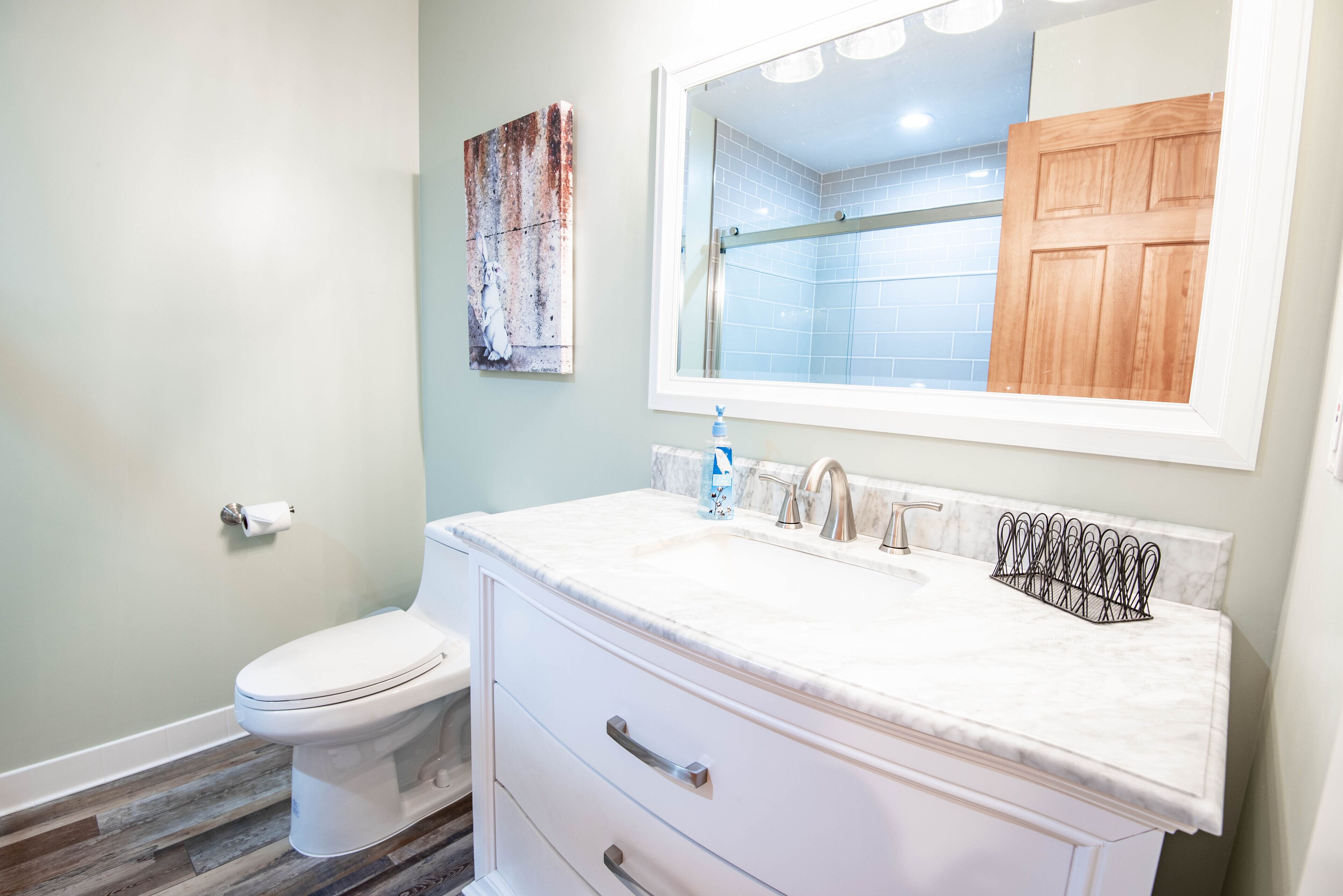 A bathroom with a toilet, a sink with a marble countertop, a mirror, and a wooden door.
