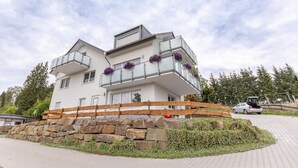 Uma casa moderna de dois andares com fundação de pedra, cerca de madeira e um carro estacionado na entrada.