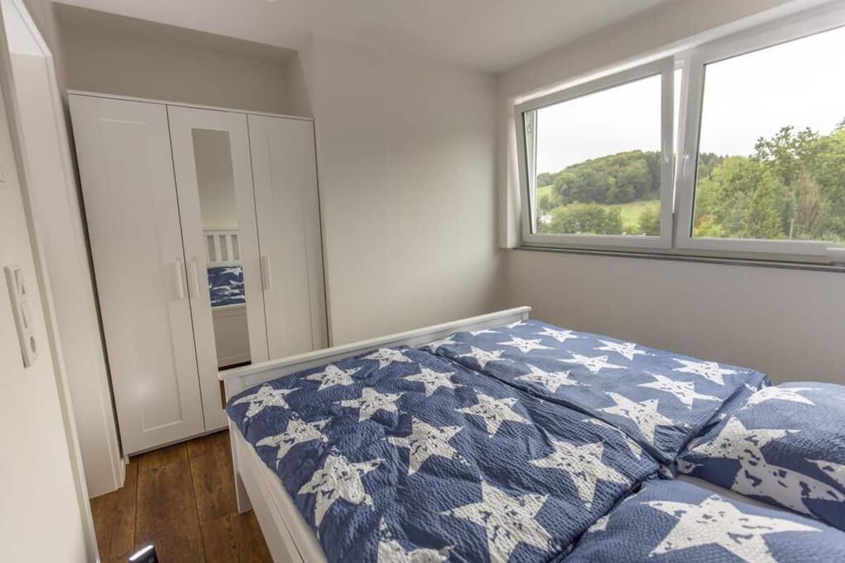 A bedroom with a bed, a wardrobe, and a window with a view of greenery.