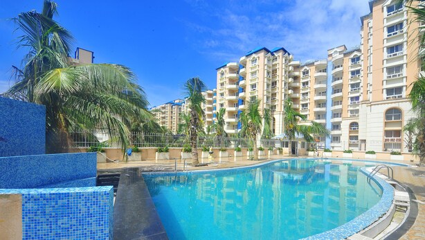 Una piscina con bordes de azulejos, rodeada de palmeras y un edificio de varios pisos con balcones.