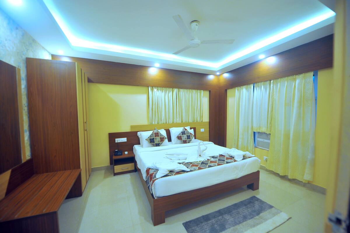 A hotel room with a bed, wooden headboard, bedside tables, a bench, and a ceiling fan.