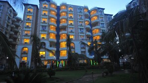 Un hotel de varios pisos con balcones, un jardín bien cuidado y un cielo despejado.