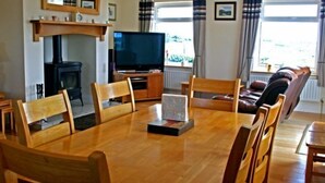 Ein gemütliches Wohnzimmer mit Holzesstisch, Stühlen, Fernseher, Kamin und einer Couch.