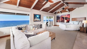 Un salón amplio con un ventanal grande con vistas al océano, un ventilador de techo y una zona de estar acogedora.