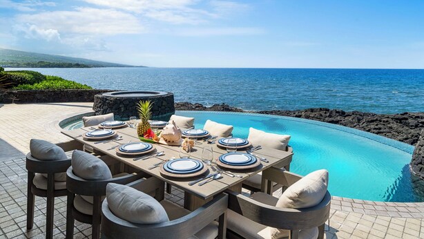 Un área de comedor al aire libre con piscina, asientos de piedra y vista al océano.