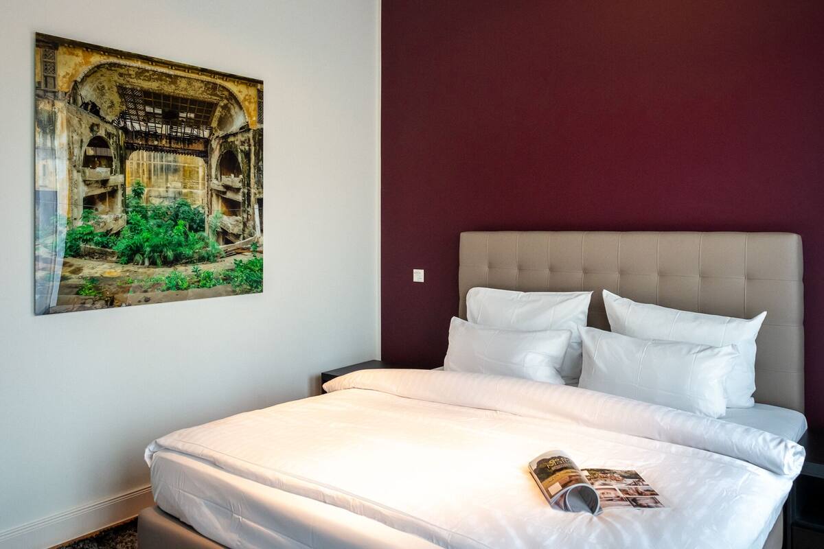 Quarto com cama, almofadas, uma revista e um pôster na parede.