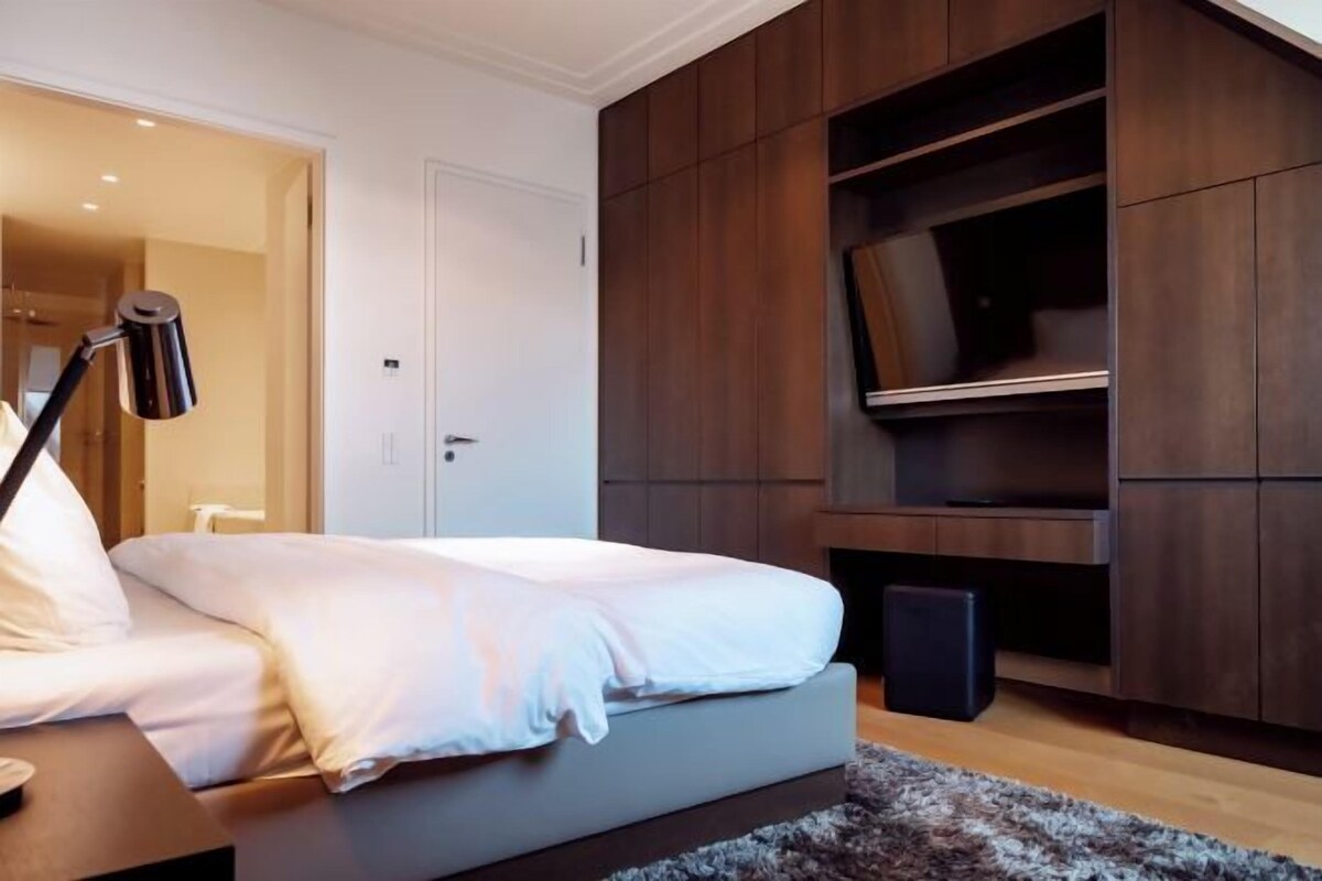 Un dormitorio moderno con una cama, un escritorio, una lámpara y estanterías empotradas de madera.