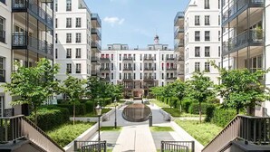 Un moderno complejo de apartamentos con un patio central, varios balcones y un edificio destacado con una torre.