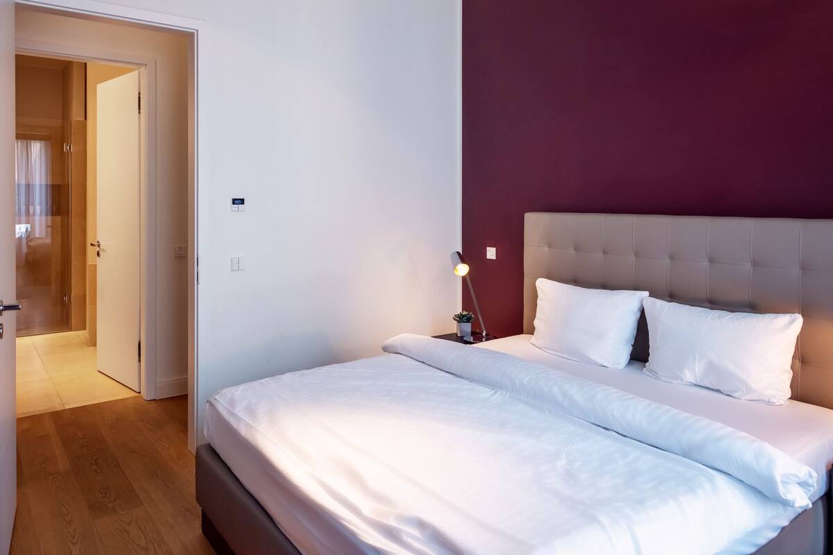 Quarto de hotel com cama, mesa de cabeceira, abajur e porta para um banheiro.