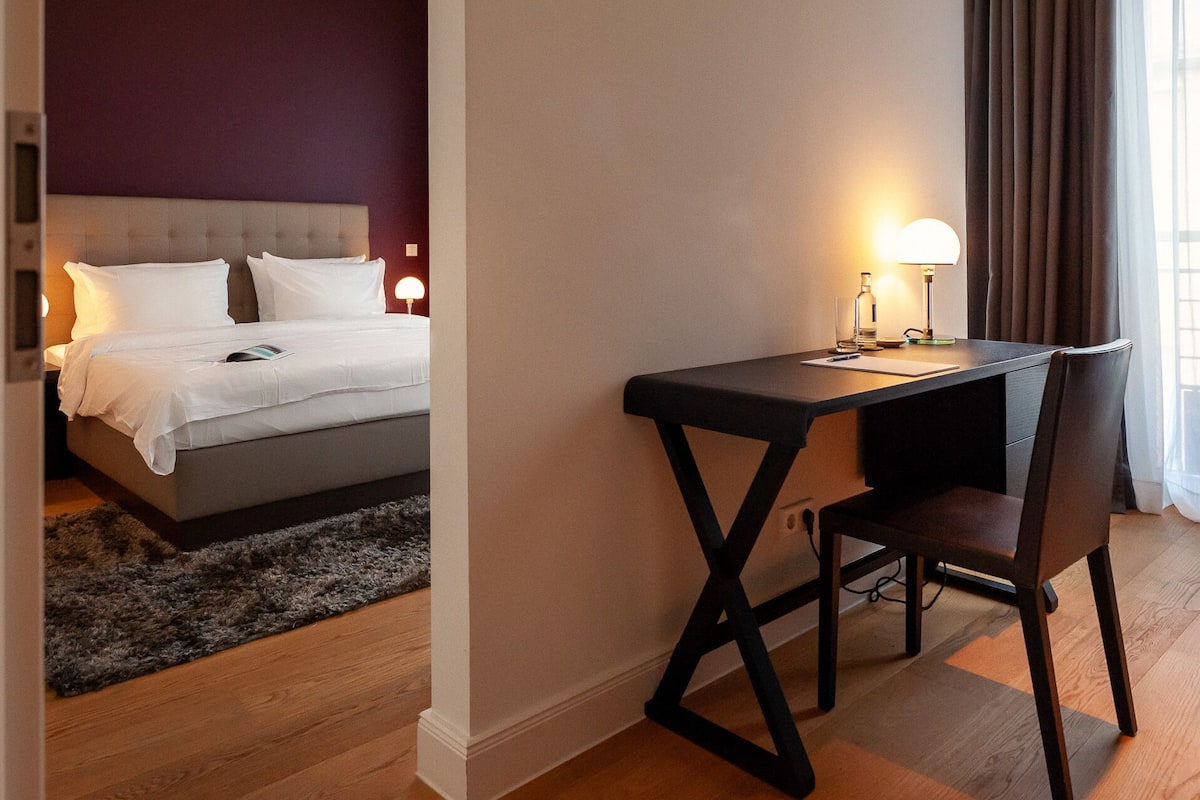 Quarto de hotel com uma cama, uma escrivaninha e uma cadeira.