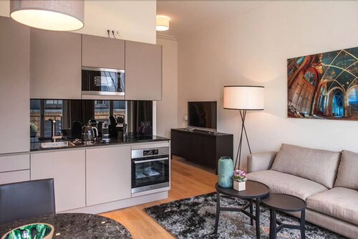 Uma cozinha moderna com eletrodomésticos embutidos, uma sala de jantar com mesa de mármore e uma sala de estar com sofá e um quadro.