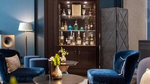 Una sala moderna con sofás de terciopelo azul oscuro, una mesa de centro redonda y una zona de bar con varias botellas.