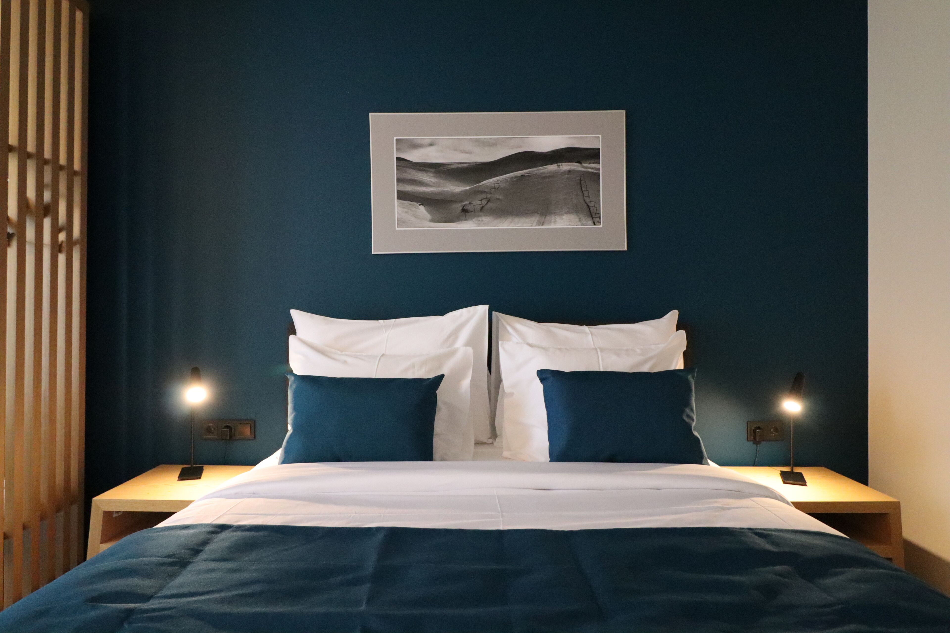 A neatly made bed with white and blue bedding, two bedside tables with lamps, and a framed picture on the wall.