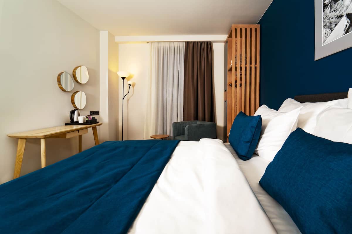 Una habitación de hotel con cama, escritorio, silla, lámpara y armario.
