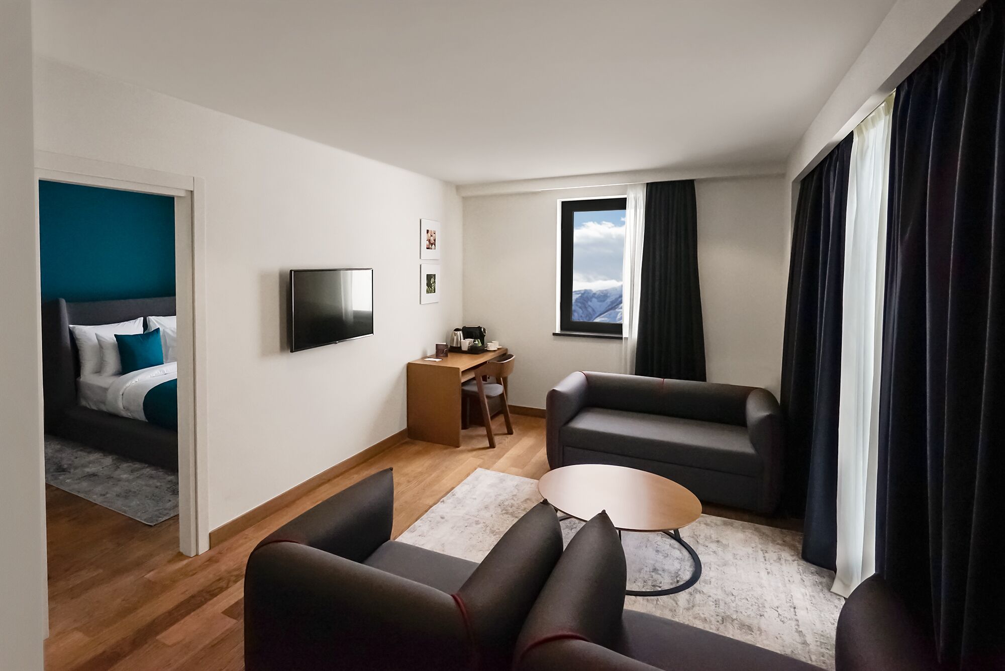 A modern hotel room with a bed, a TV, a sofa, a coffee table, and a desk.