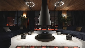 A modern lounge area with a central fire feature, dark sofas, and a patterned rug. - Gudauri Lodge (Kazbegi)