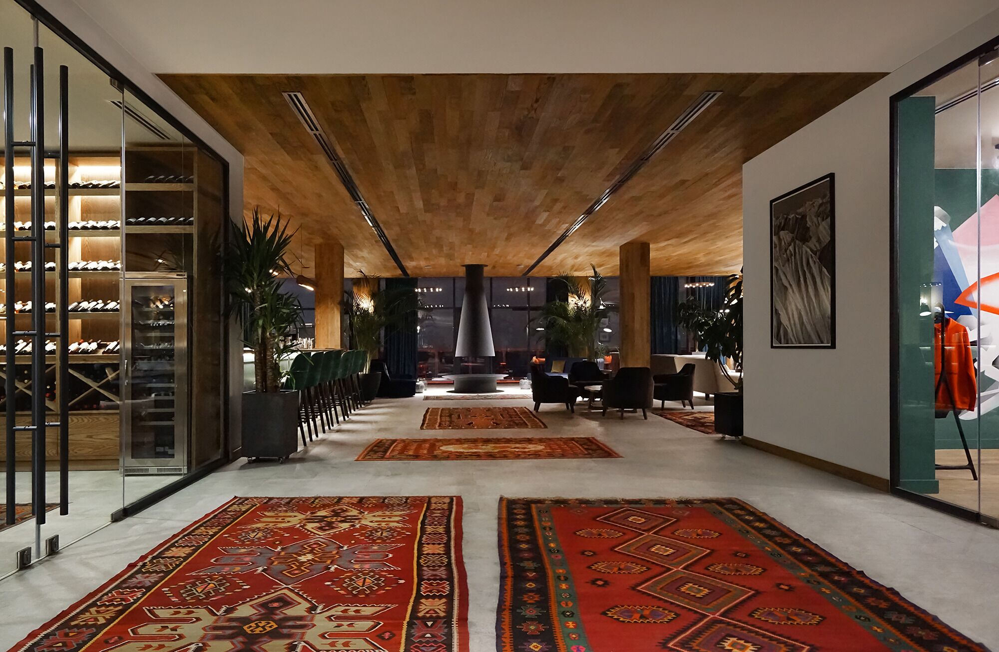 A spacious lobby with a high ceiling, a central seating area, and a wine rack on the left.
