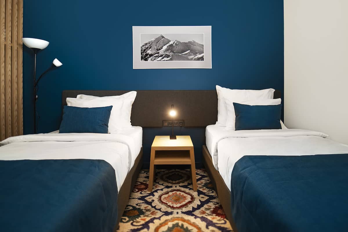 Una habitación de hotel con dos camas, una mesita de noche, una lámpara y un cuadro en la pared.