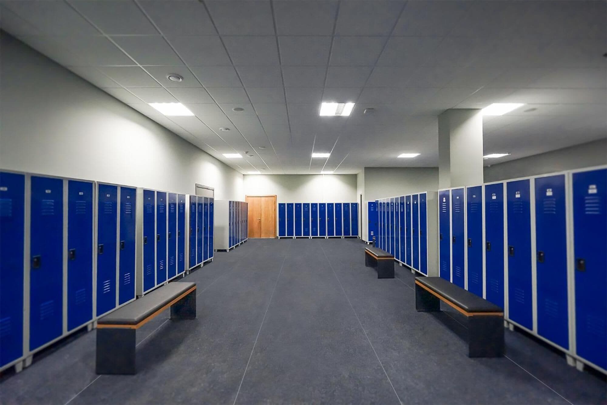 A locker room with blue lockers, benches, and a wooden door at the end.