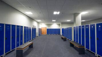 A locker room with blue lockers, benches, and a wooden door at the end.