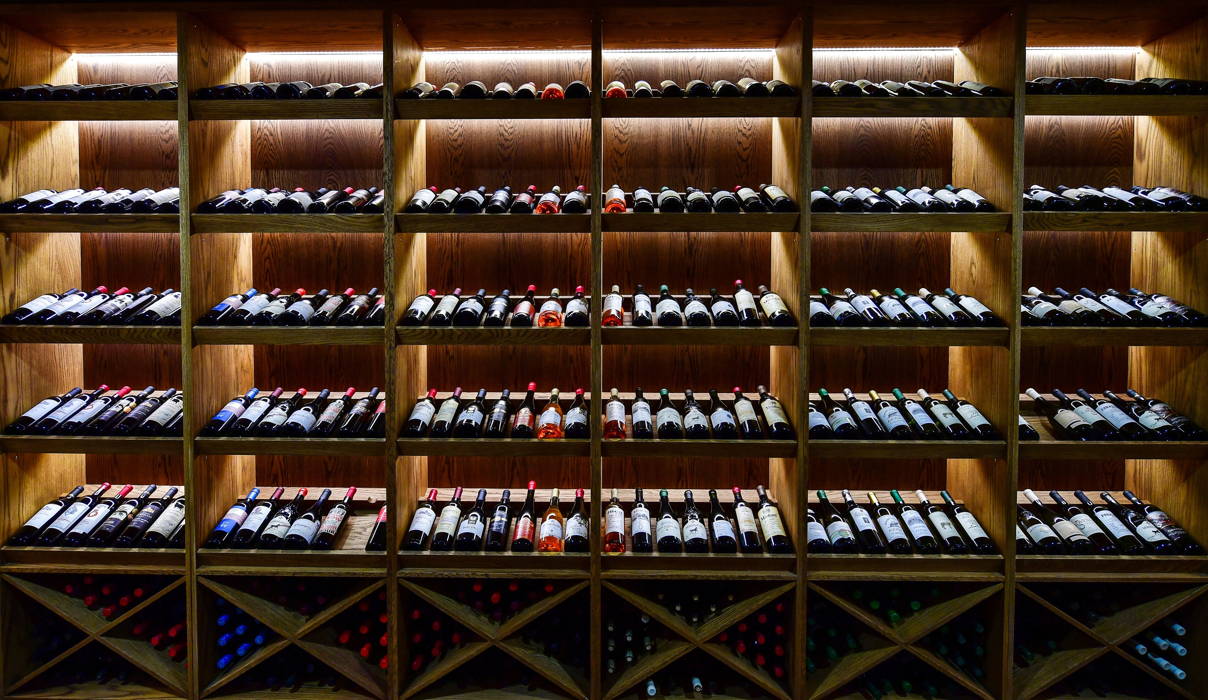 A wine cellar with multiple wooden shelves holding bottles of wine.