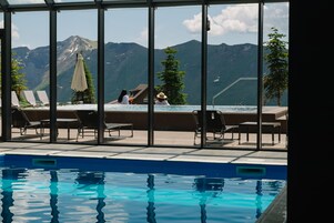 Una piscina interior con vistas nítidas a la montaña, sillas de descanso y un pequeño edificio con techo.