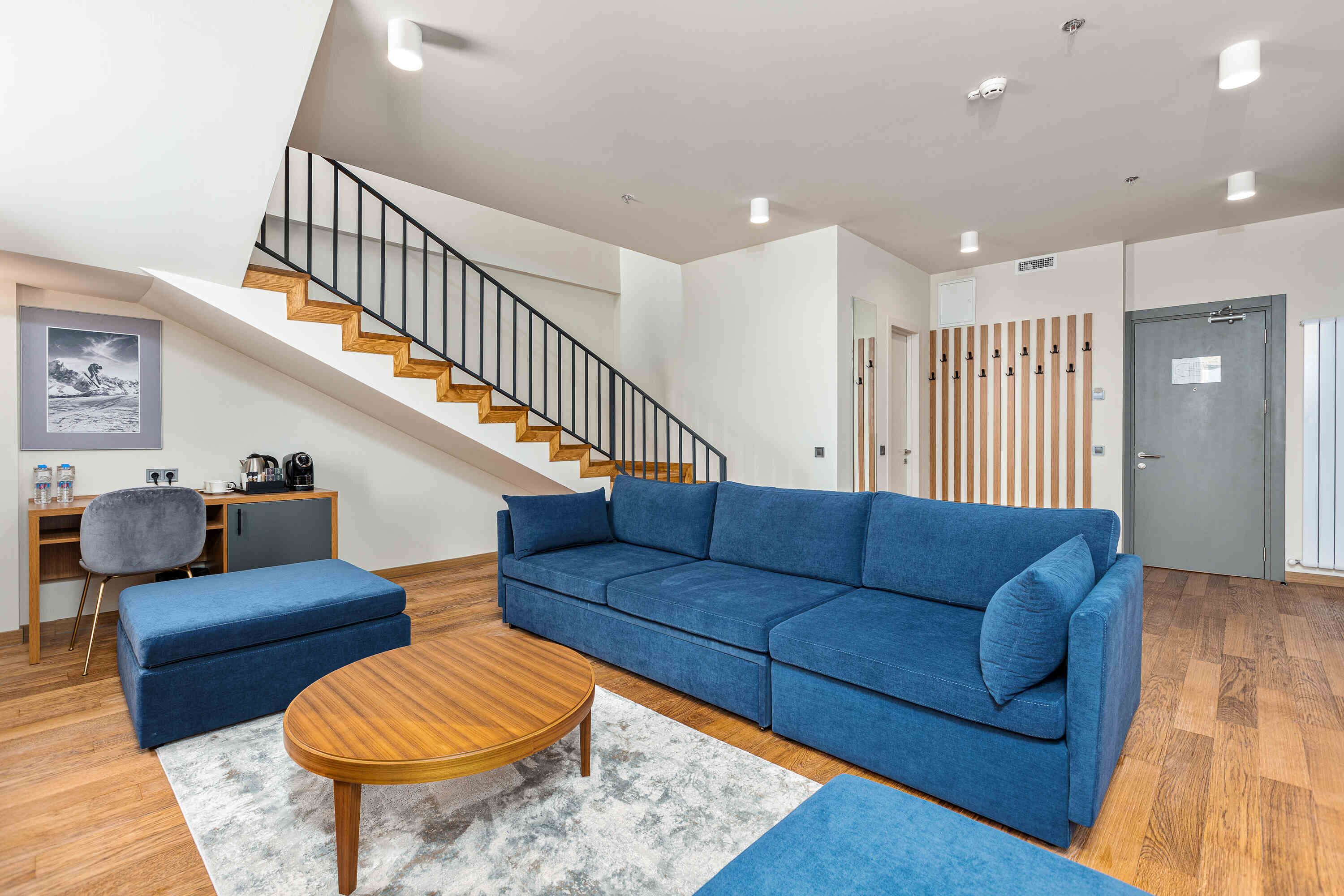 A modern living room with a blue sofa, wooden coffee table, and a staircase.