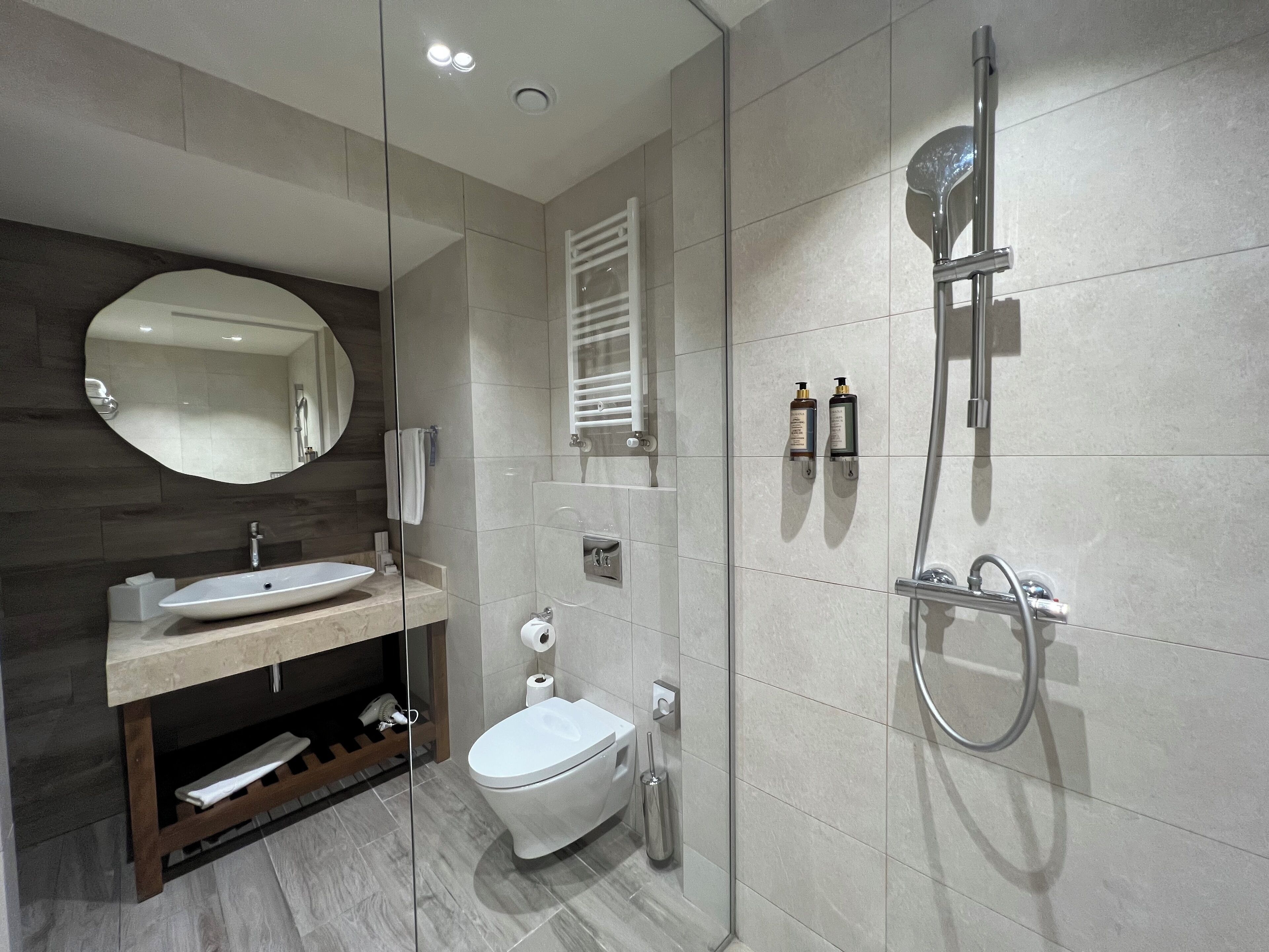 A modern bathroom with a glass-enclosed shower, a round mirror, a sink, and a toilet.