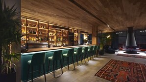 A bar area with a long counter, multiple shelves of bottles, and green bar stools. - Gudauri Lodge (Kazbegi)
