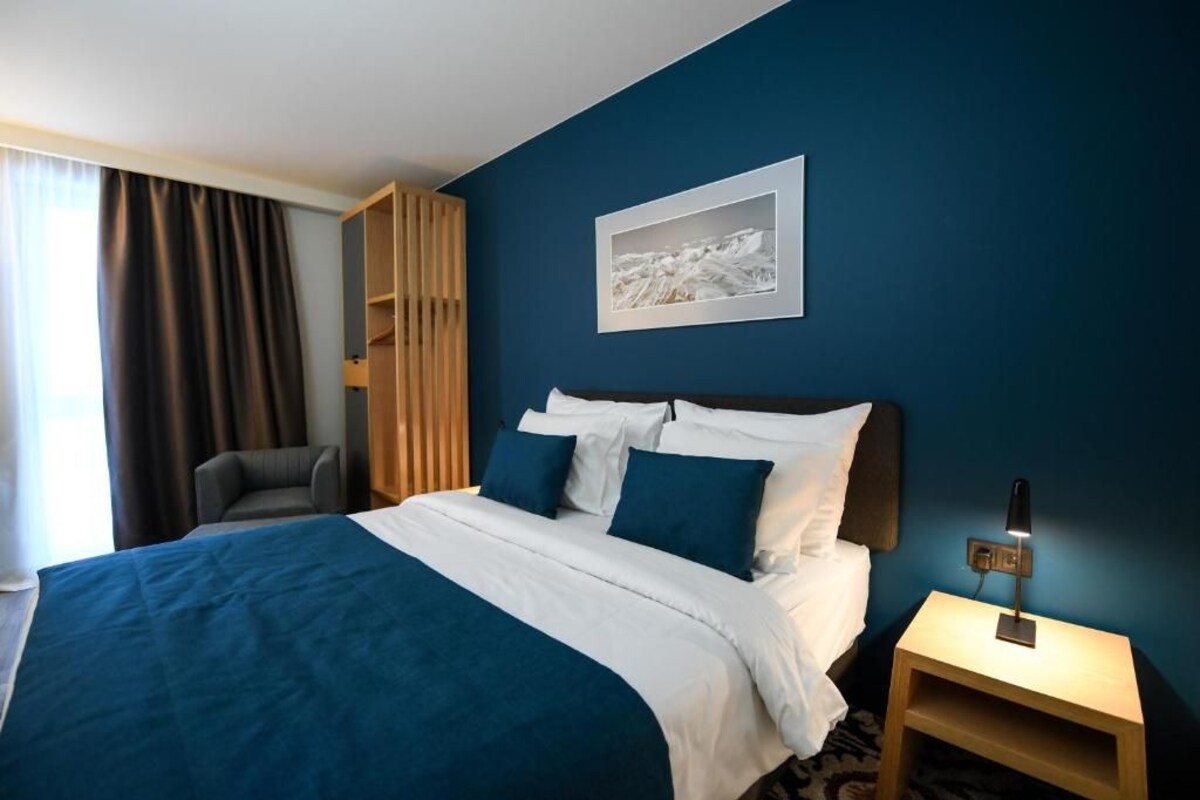 A hotel room with a bed, a chair, a nightstand, a lamp, and a picture on the wall.