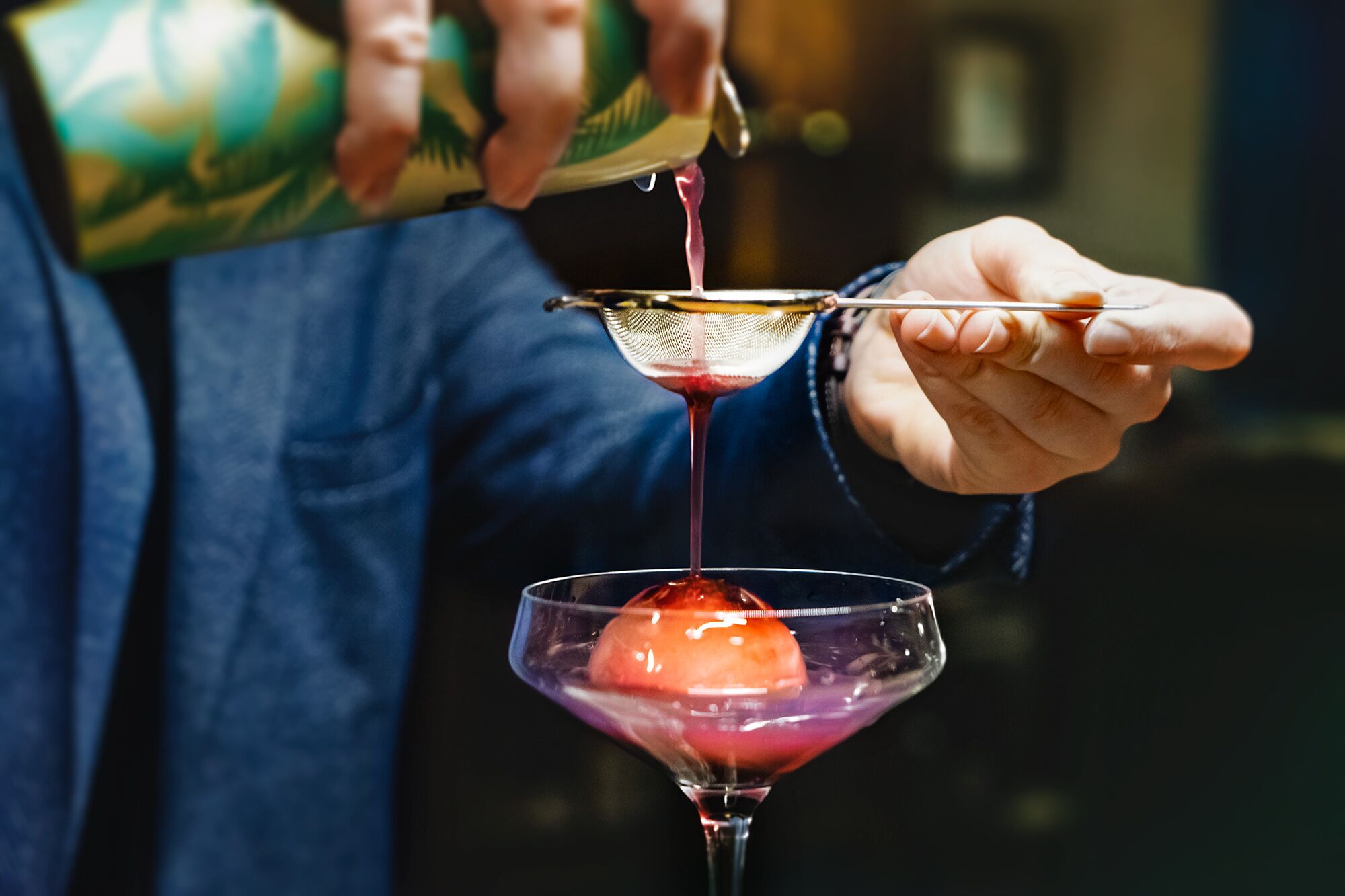 A person pouring a pink liquid into a martini glass.