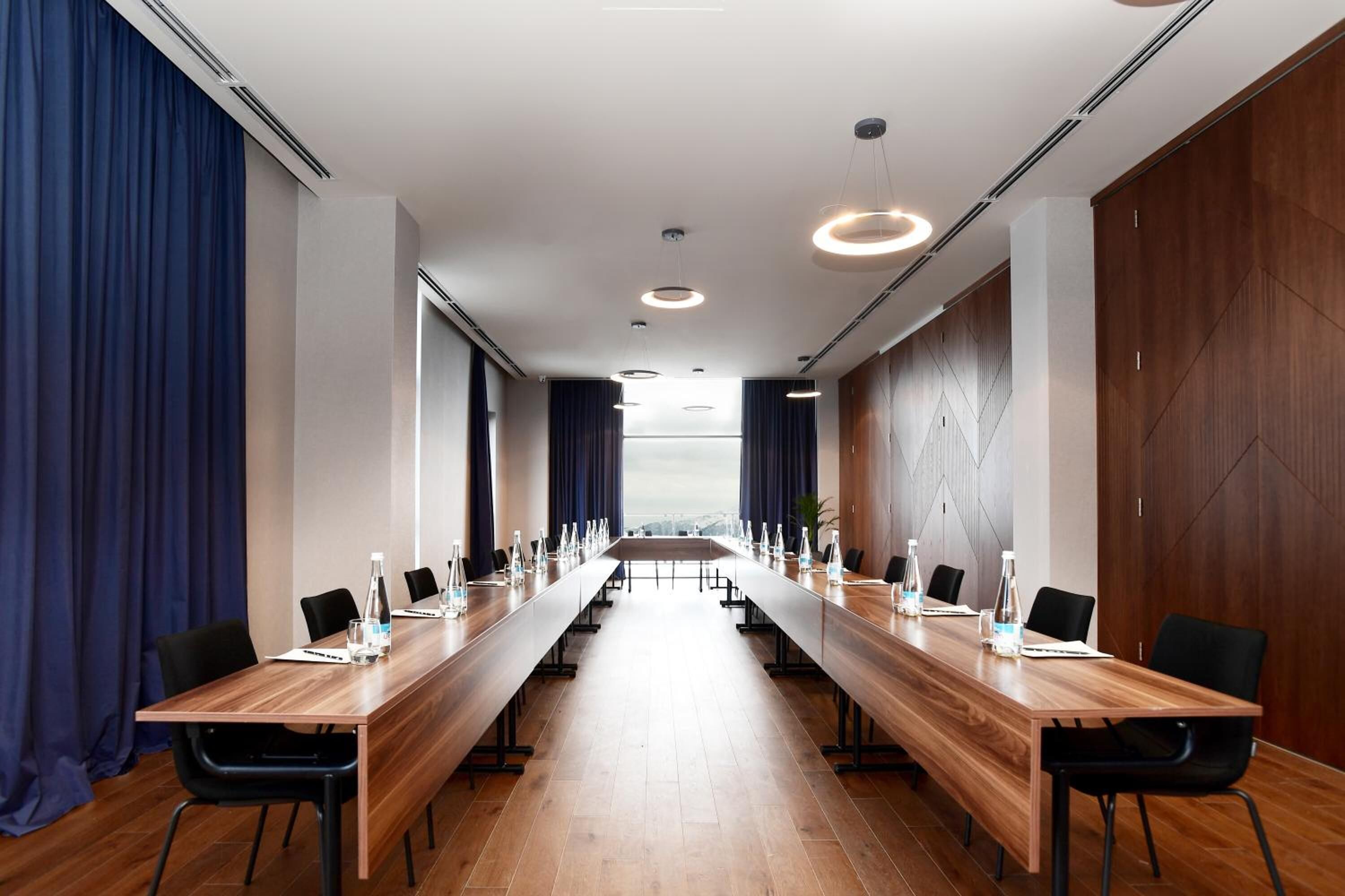 A conference room with a long wooden table, black chairs, and a view through the windows.
