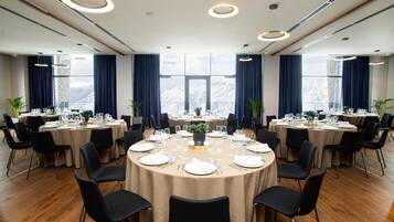 Uma sala de conferências com mesas redondas, cadeiras pretas e vista para montanhas através de amplas janelas.