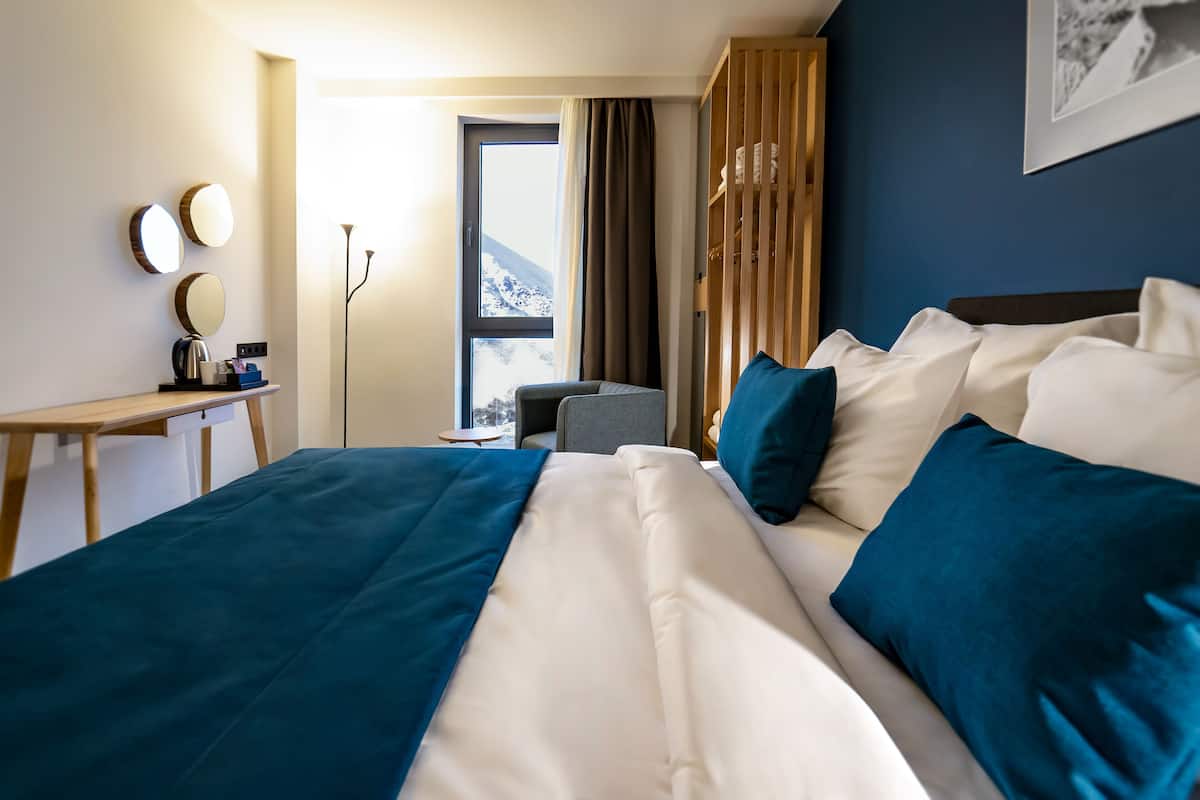 Habitación de hotel con cama, escritorio y silla. Se ve una ventana con vistas a la montaña.