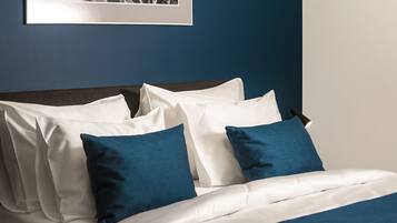 Una cama bien hecha con ropa de cama blanca y azul, un cabecero oscuro y un cuadro enmarcado en la pared.
