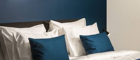 Una cama bien hecha con ropa de cama blanca y azul, un cabecero oscuro y un cuadro enmarcado en la pared.