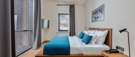 A modern hotel room with a large bed, a small bedside table, a window with curtains, and a wall-mounted TV.