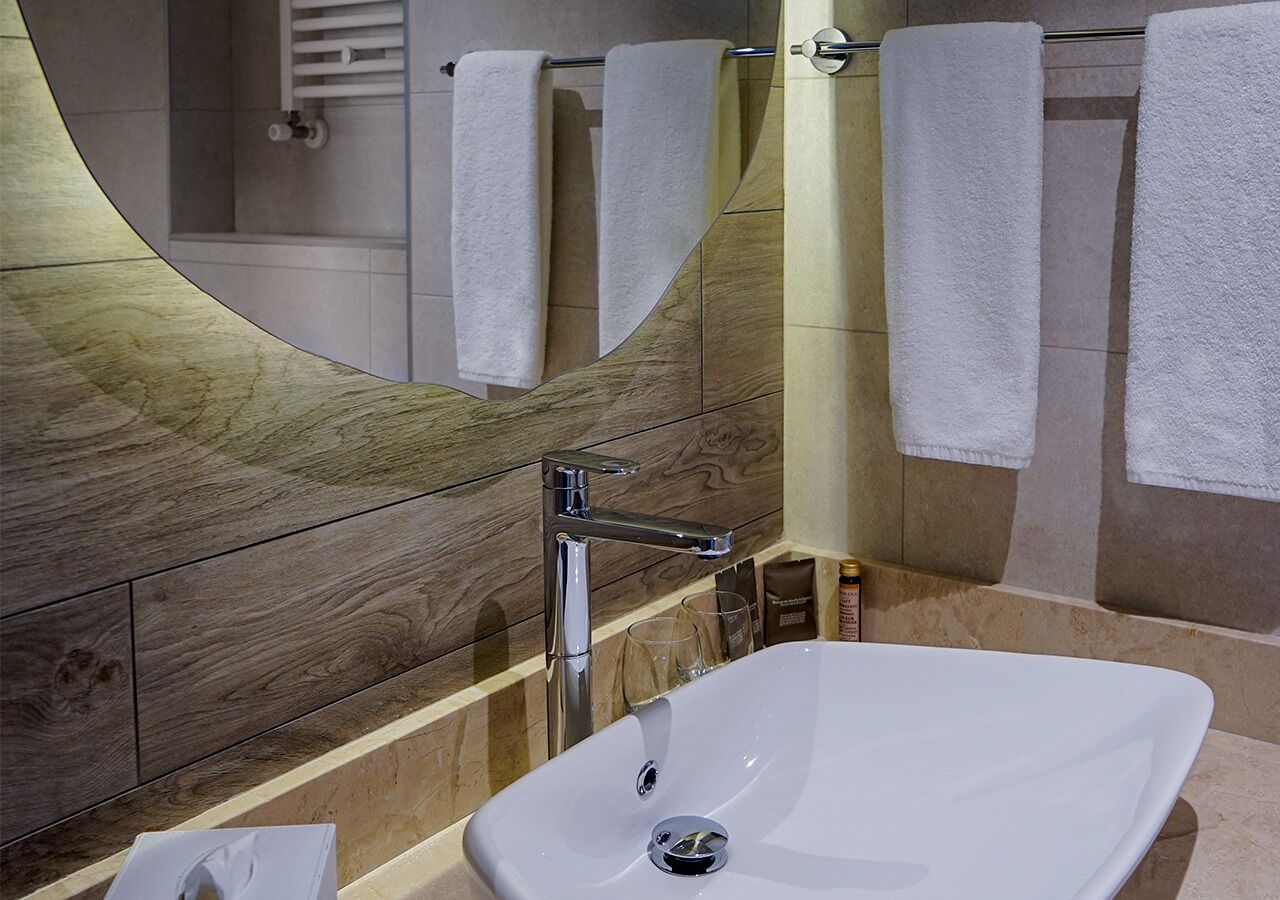 A modern bathroom with a large mirror, a chrome faucet, and a white sink.