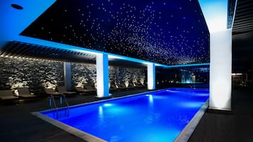 Un área de piscina interior moderna con techo estrellado, paredes de piedra y sillones de descanso.