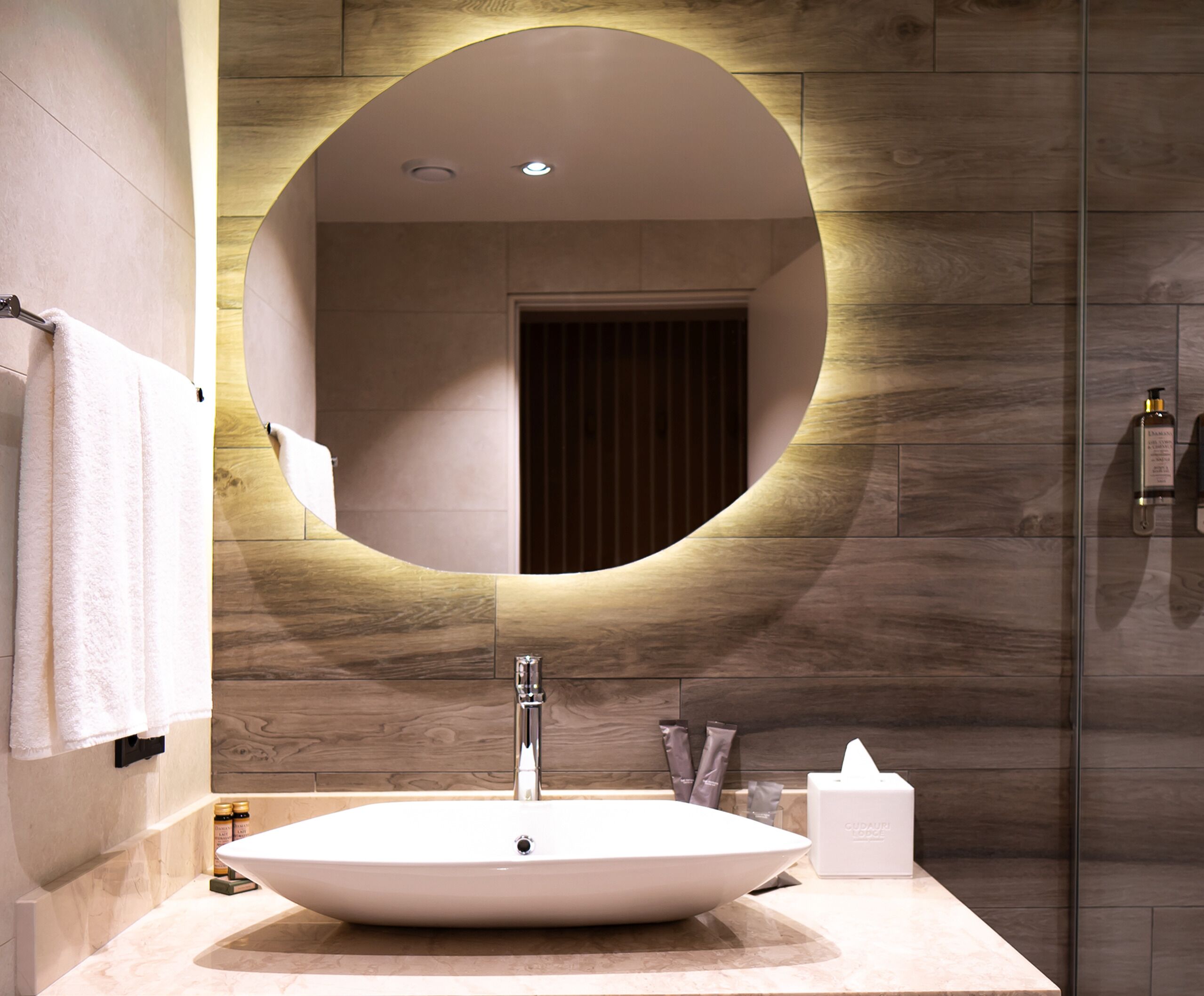Un baño moderno con un espejo ovalado grande, un lavamanos blanco y paneles de madera en las paredes.