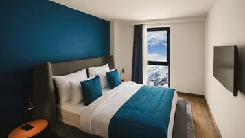 Une chambre d’hôtel moderne avec un grand lit, une vue sur des montagnes enneigées et un téléviseur fixé au mur.