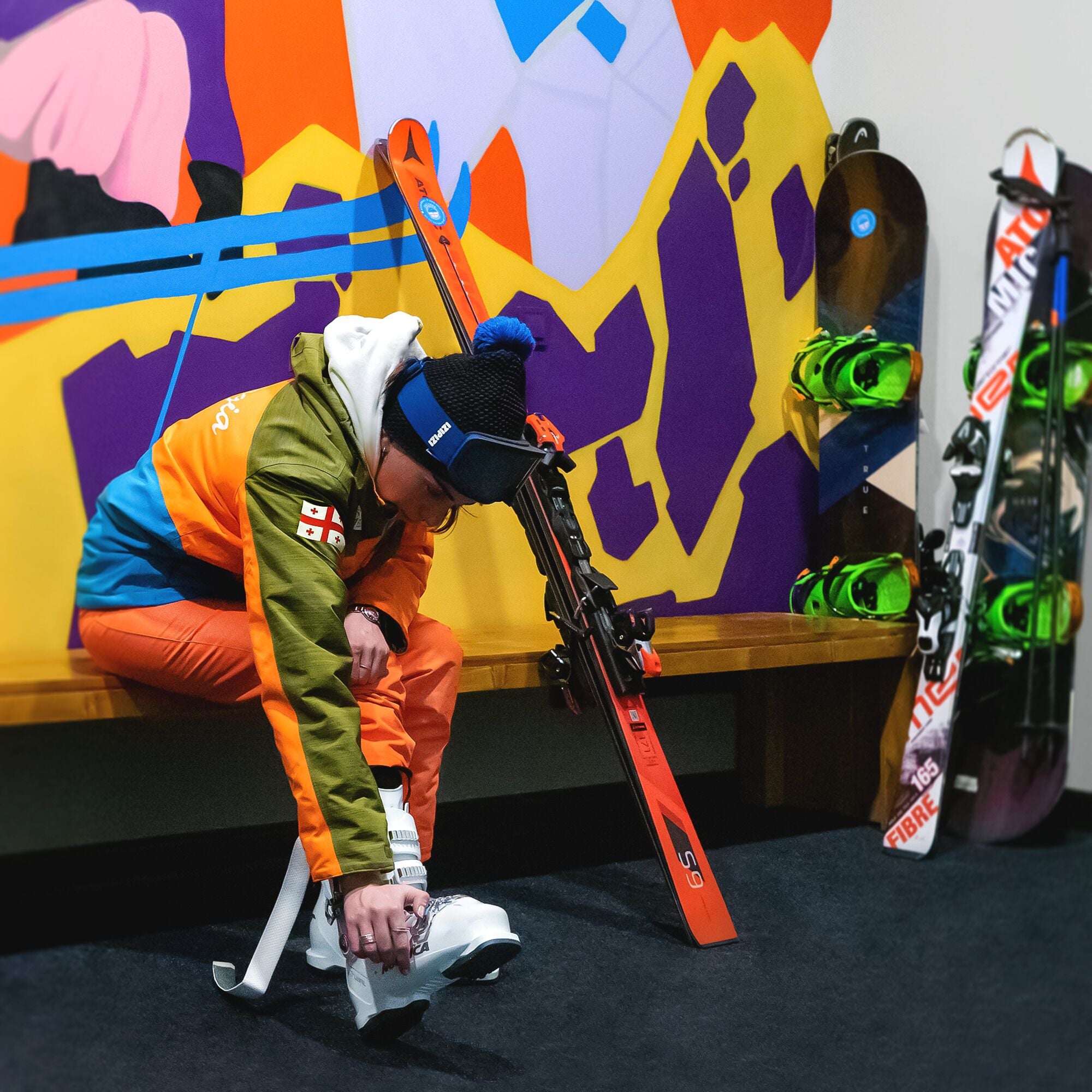 A person adjusting ski boots in a room with skis and ski equipment.
