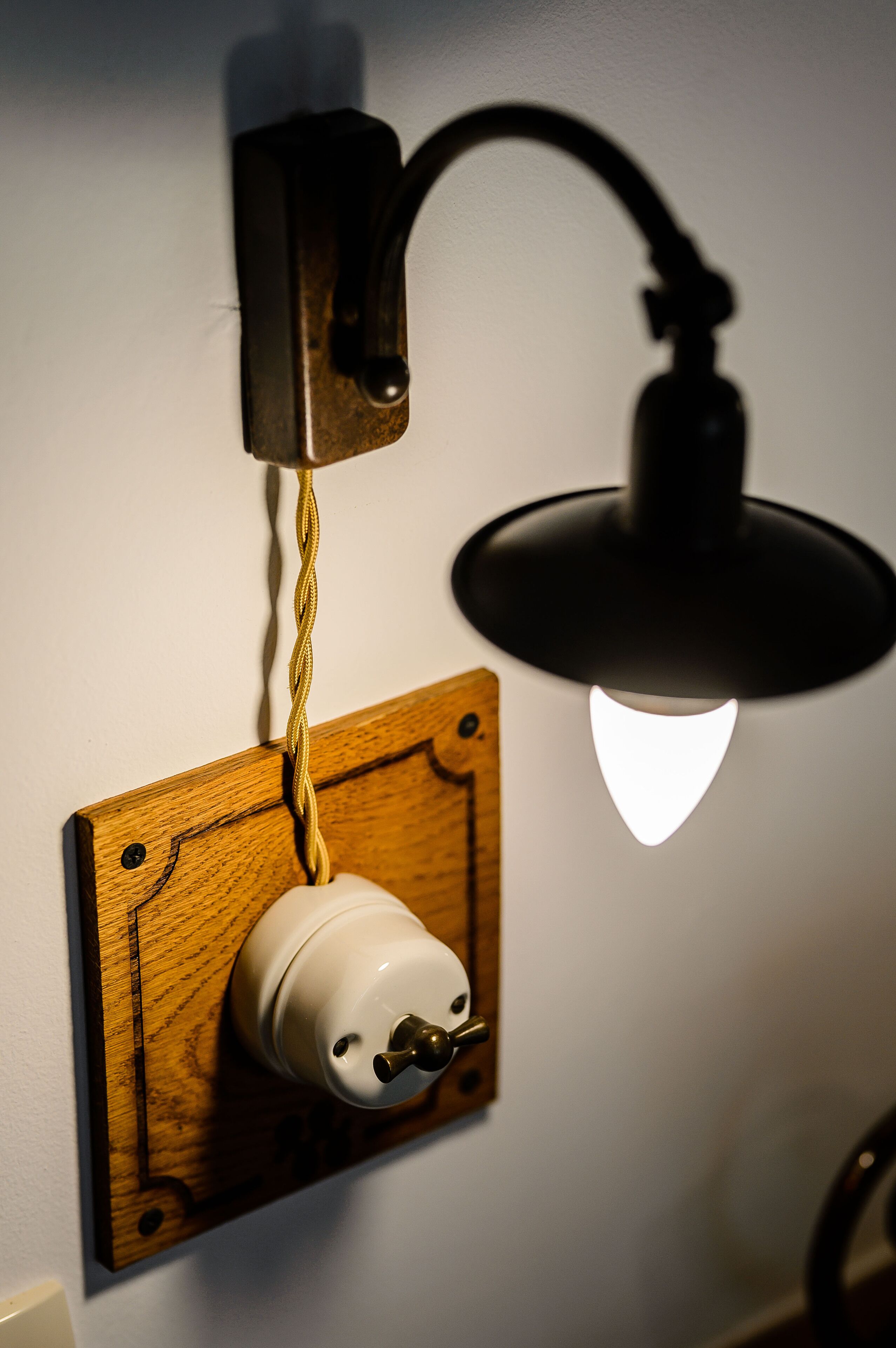 Toma corriente empotrada en una pared con un panel de madera, un enchufe blanco y una lámpara negra con bombilla blanca.