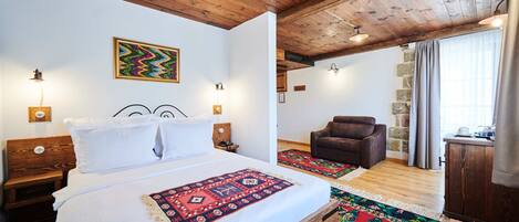A bedroom with a wooden ceiling, a bed with a patterned bedspread, a chair, and a stone wall.