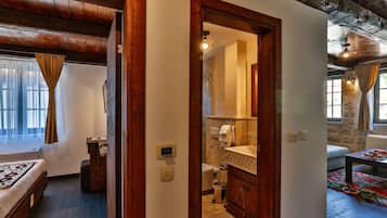 Una habitación con techo de madera, una cama, un baño con pared de piedra y un comedor con mesa y sillas.