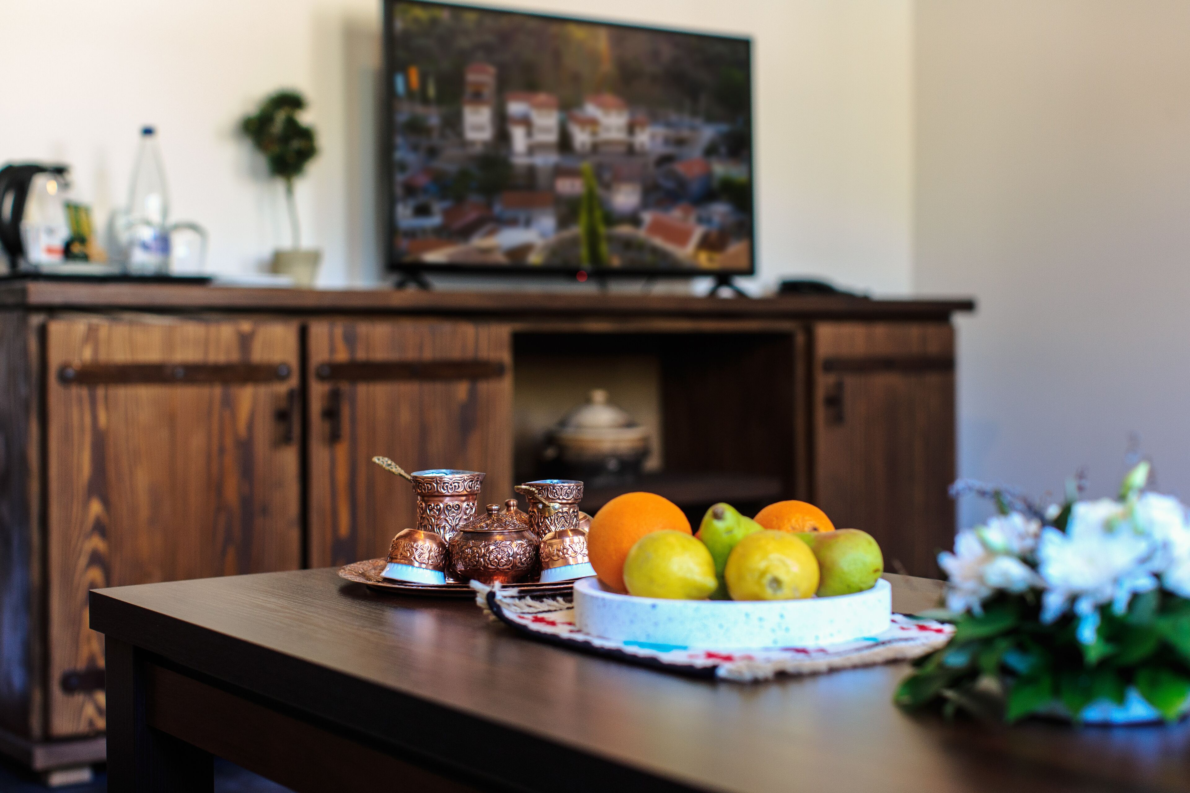 A wooden table with a fruit bowl, a decorative tray, and a vase of flowers.