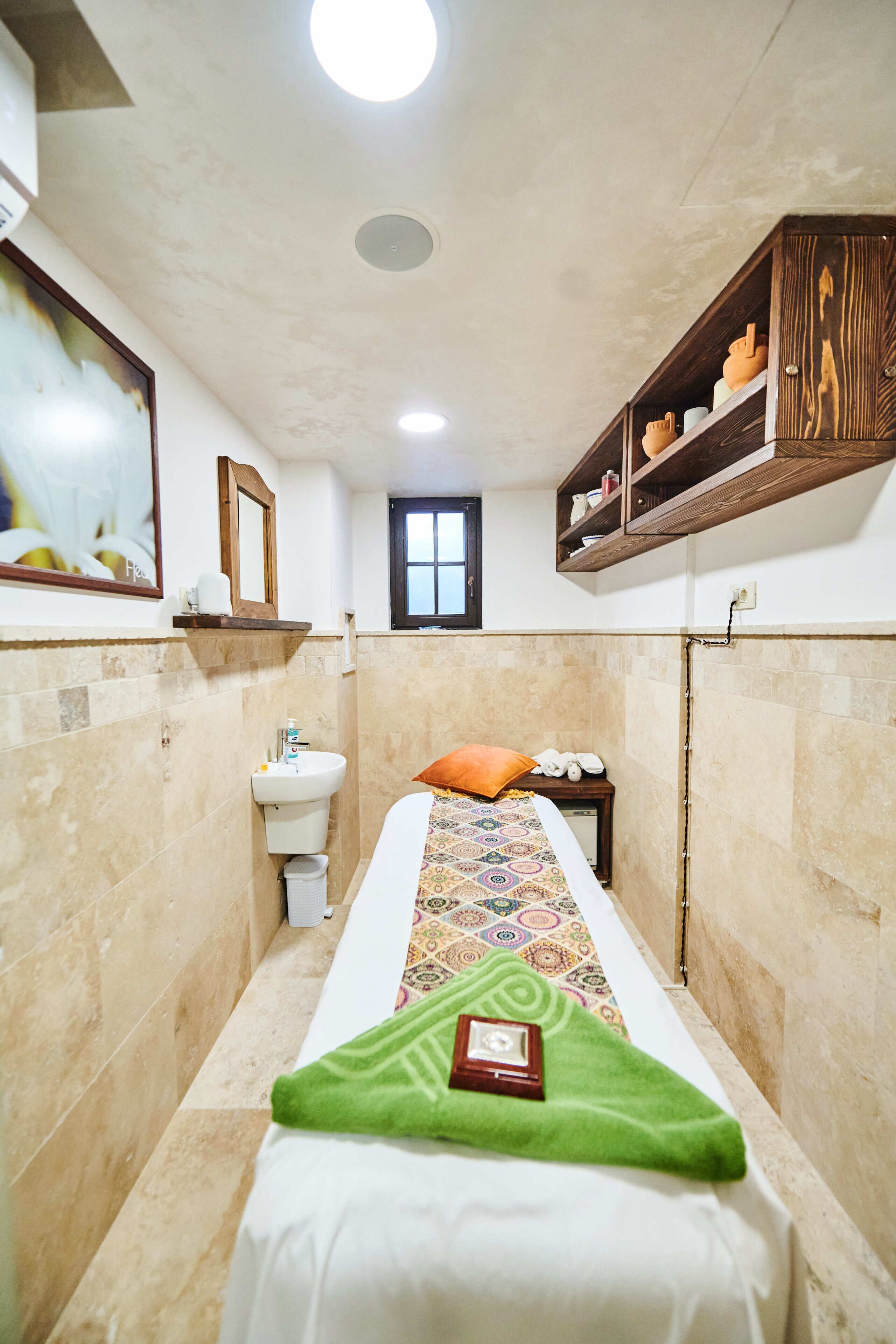 Una habitación de hotel estrecha con una cama individual, una ventana pequeña, un lavamanos y un estante de madera sobre la cama.