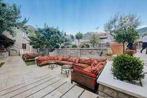 An outdoor seating area with sofas and tables, surrounded by stone walls and potted plants.