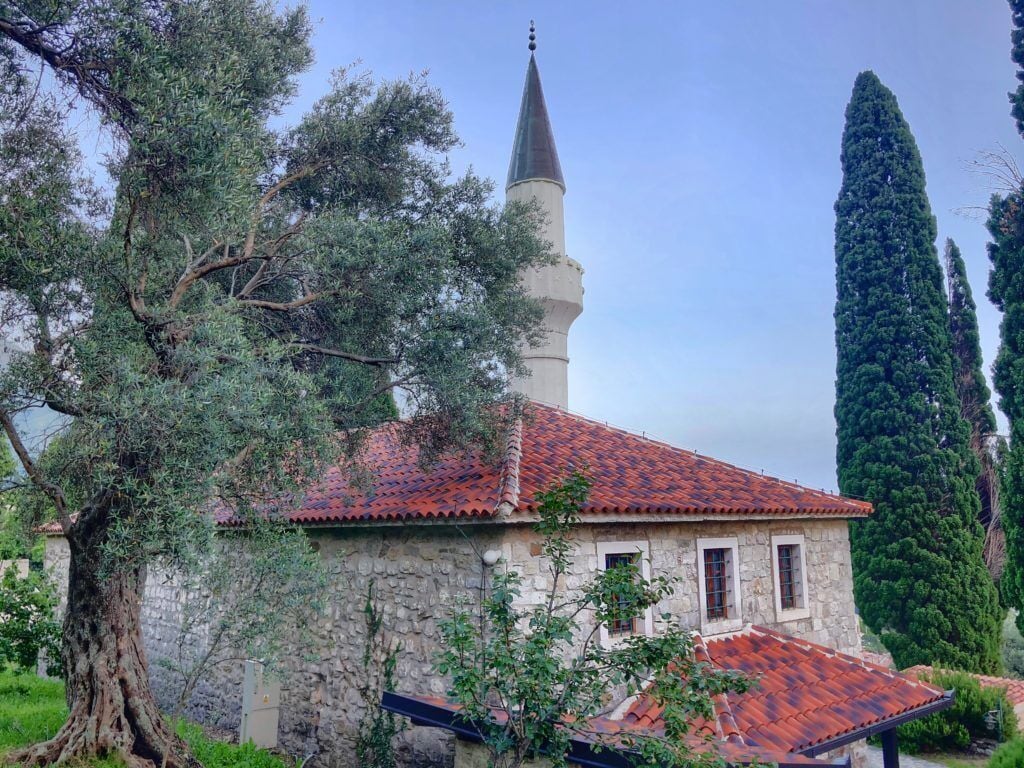 A stone building with a red-tiled roof and a tall, narrow tower.